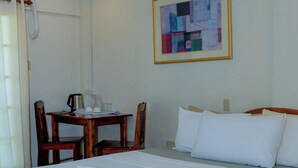 A hotel room with a bed, a desk with a chair, a coffee maker, and a framed abstract painting on the wall. - Villa Paraiso Resort and Waterpark Camiguin (Mambajao)