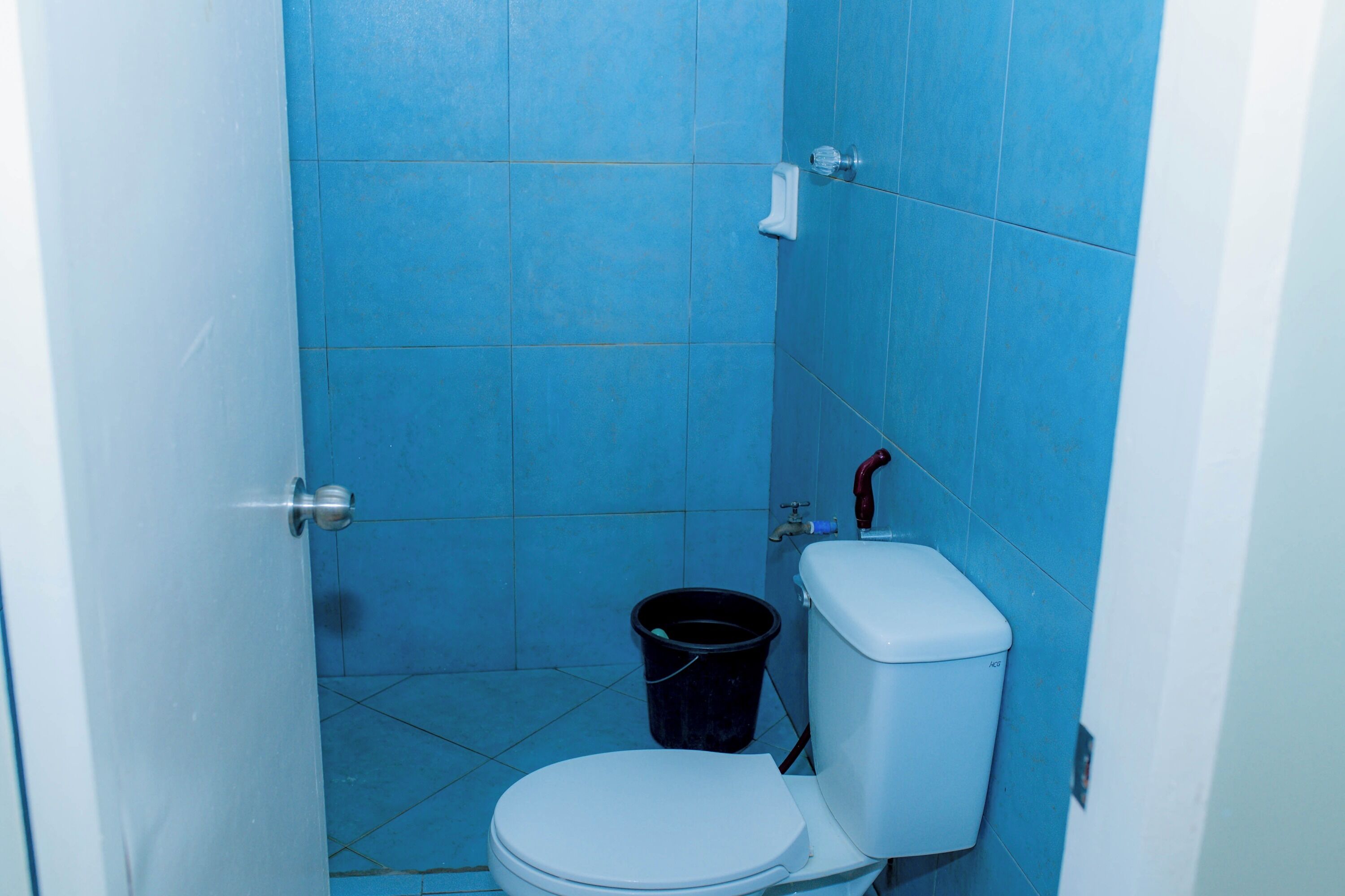A small, compact bathroom with a white toilet, a black bucket, and blue tiles on the walls.
