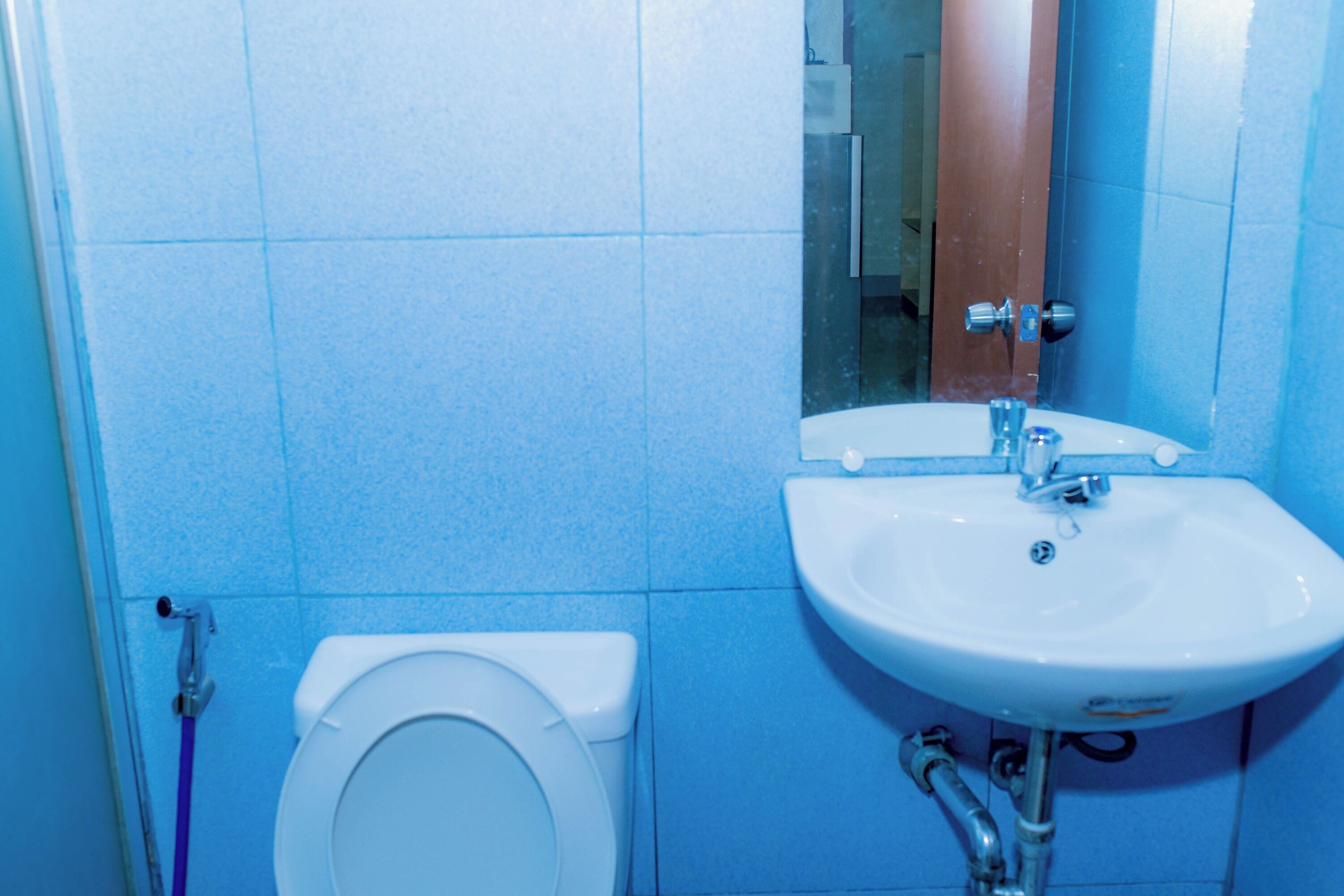 Un baño con inodoro y lavamanos blancos, paredes con azulejos azules y un espejo sobre el lavamanos.