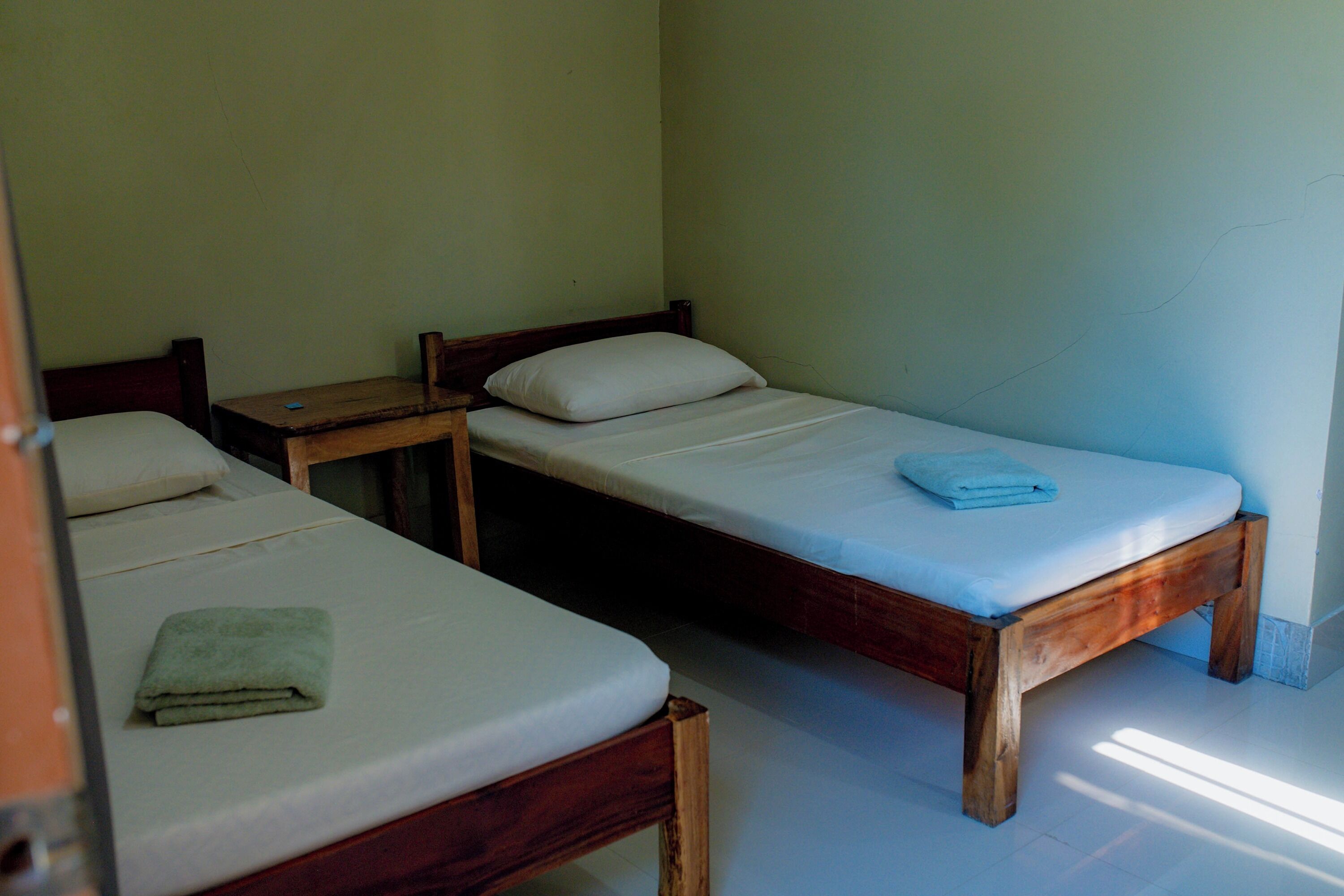 A simple room with two wooden beds, each with a pillow and a folded towel.