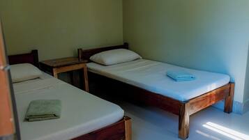 A simple room with two wooden beds, each with a pillow and a folded towel.