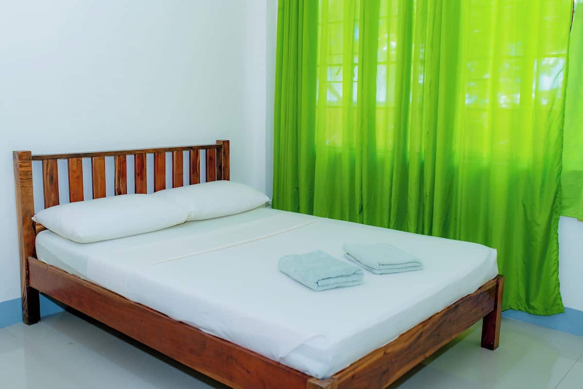Una cama individual con estructura de madera, ropa de cama blanca y dos toallas dobladas.