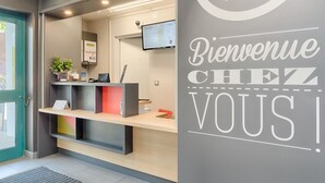 A hotel reception area with a digital screen, a reception desk, and a welcome sign. - B&B HOTEL AIX EN PROVENCE Pont de l'Arc (Aix-en-Provence)