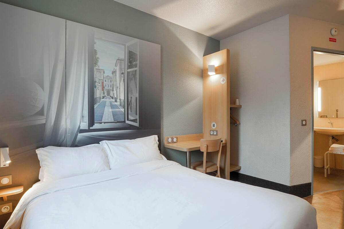 A hotel room with a bed, a desk, a chair, a mirror, and a bathroom visible through an open door.