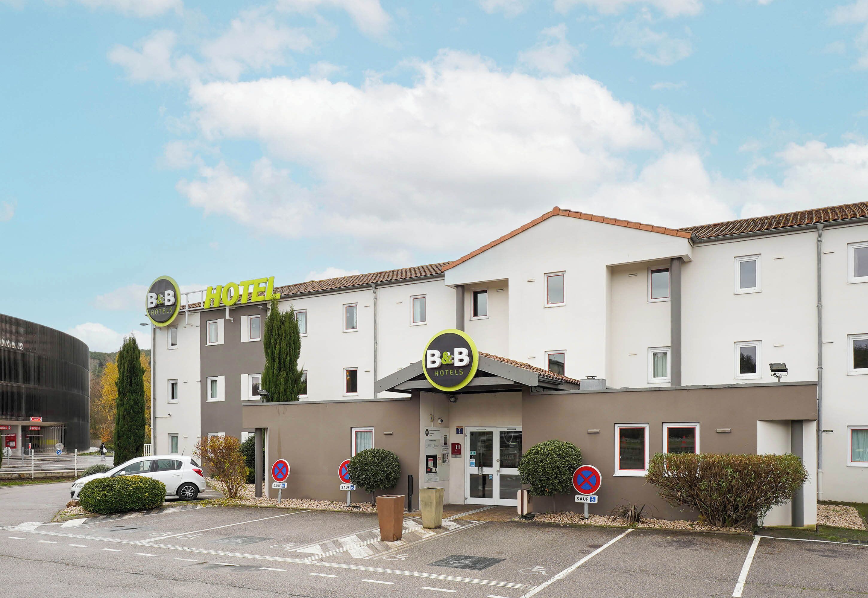 A B&B hotel with a modern facade, a parking lot, and a car parked in front.