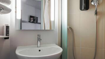Une salle de bain avec un lavabo blanc, un miroir, une douchette à main et un porte-serviettes.