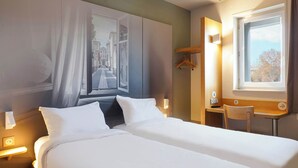 A hotel room with a bed, a desk, a chair, a window with a view, and a wall-mounted light. - B&B HOTEL AIX EN PROVENCE Pont de l'Arc (Aix-en-Provence)