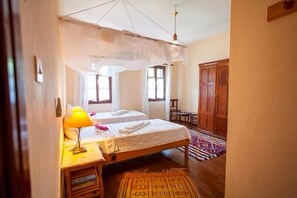 Un dormitorio con dos camas, una mesita de noche de madera con una lámpara, un tapete estampado y un armario.