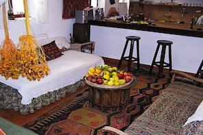 Una habitación acogedora con cama, cesta de frutas, dos taburetes y un tapete estampado.