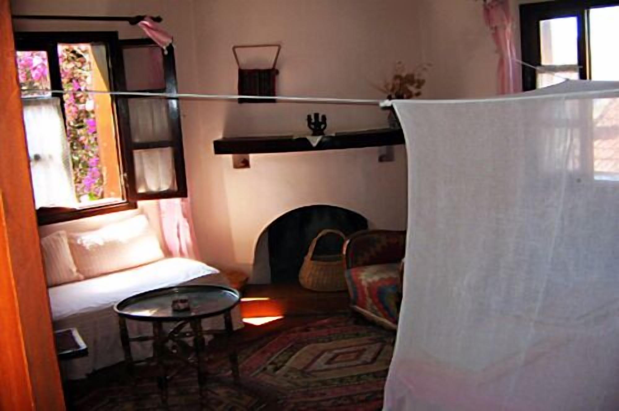 Quarto aconchegante com cama, uma mesinha redonda, uma cadeira e janela com cortinas.