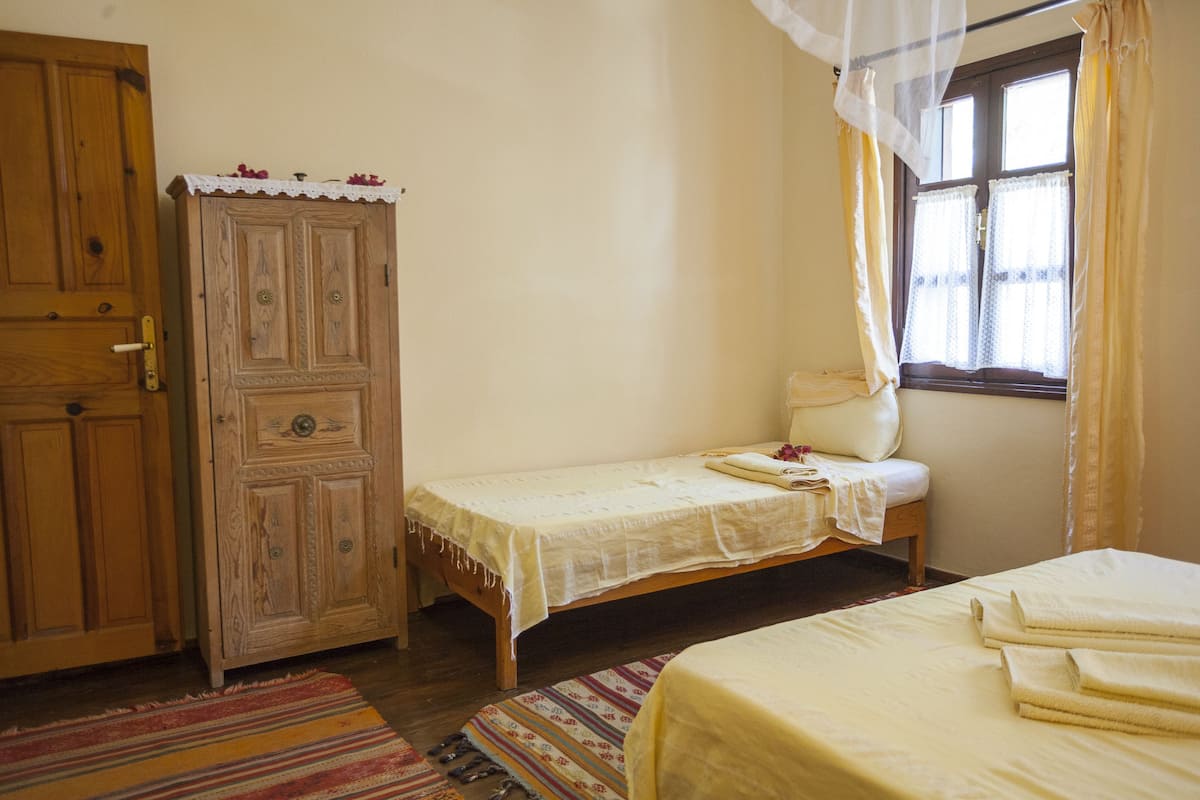 A bedroom with a single bed, a wooden wardrobe, and a window with curtains.
