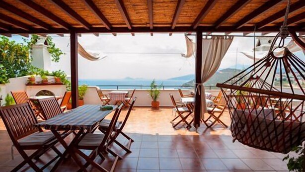 A covered outdoor seating area with a table and chairs, a hanging chair, and a view of the sea. - Turk Evi (Kas)