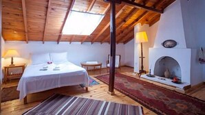 A cozy room with a wooden ceiling, a bed, a small table, a lamp, and a fireplace. - Turk Evi (Kas)