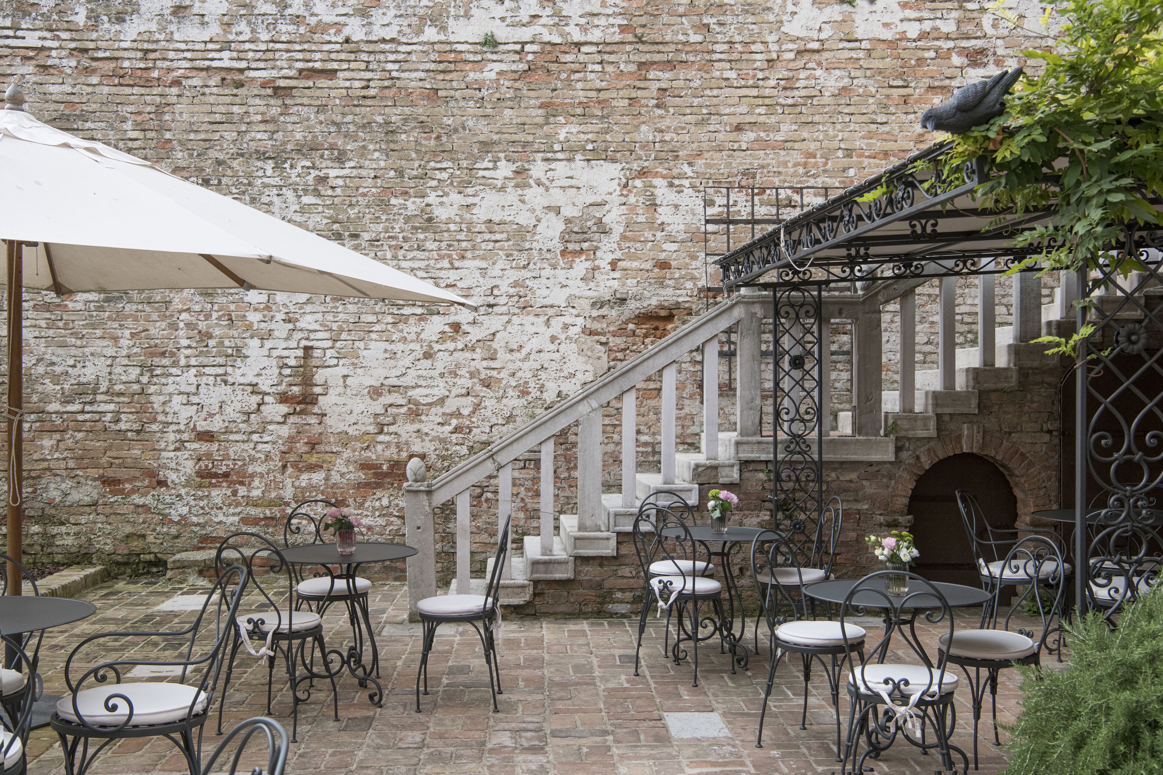 An outdoor patio with tables and chairs, a white umbrella, and a brick wall.