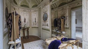 A luxurious room with ornate ceiling, a bed with gold frame, a vanity with a mirror, and a shoe rack.
