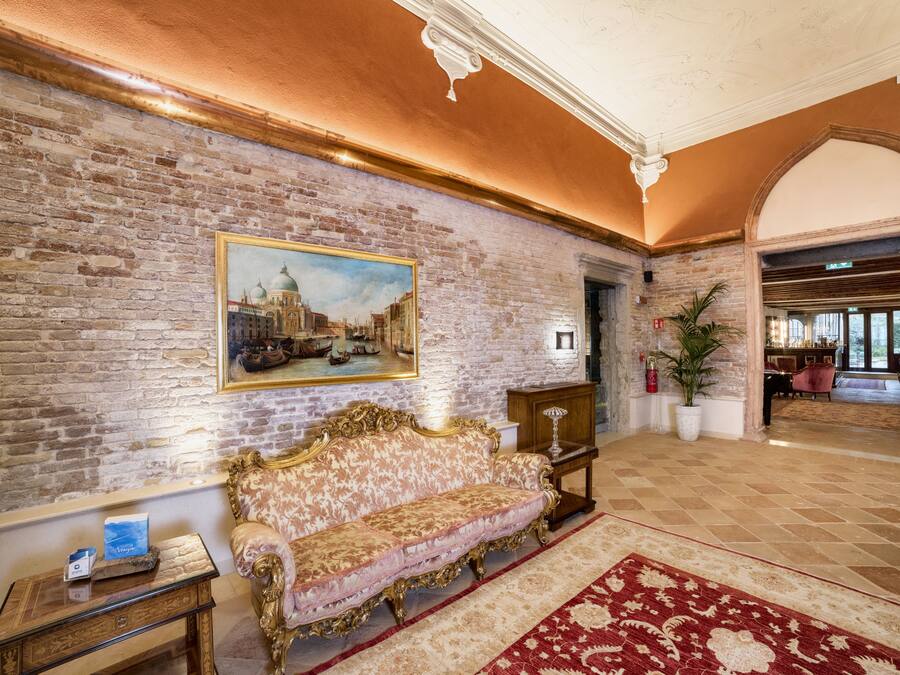 A lobby with a brick wall, a large painting, a sofa, a small table, and a red carpet.