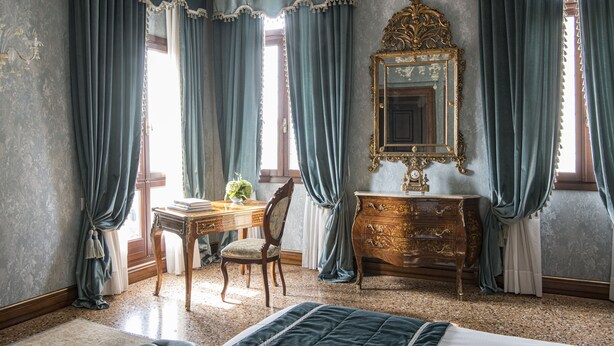 A room with a bed, a wooden dresser, a desk with a chair, and a large mirror on the wall.