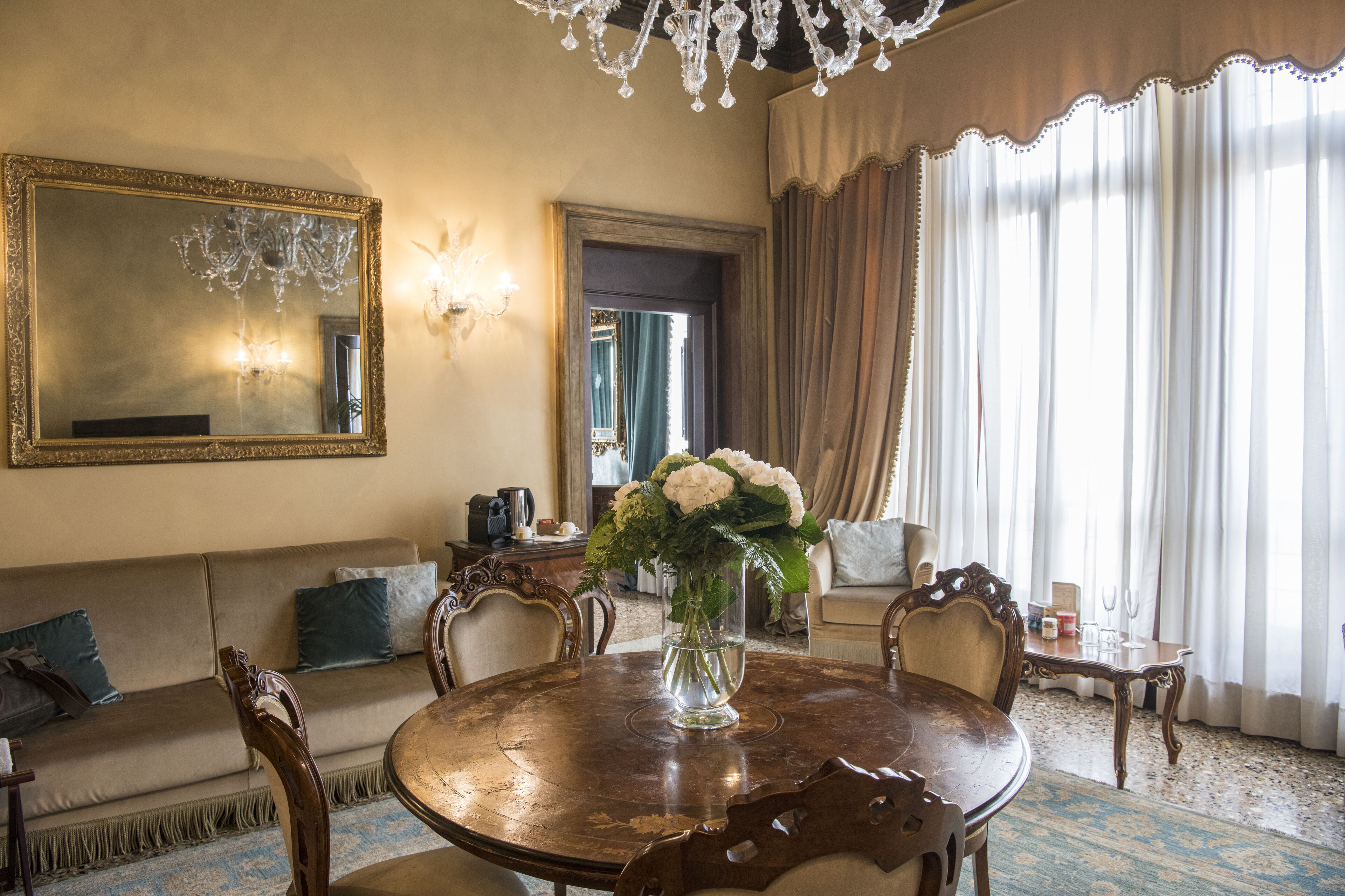 A room with a round wooden table, a sofa, a large mirror, and a chandelier.