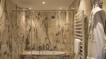 A marble bathroom with a glass-enclosed bathtub, a white towel rack, and a control panel.