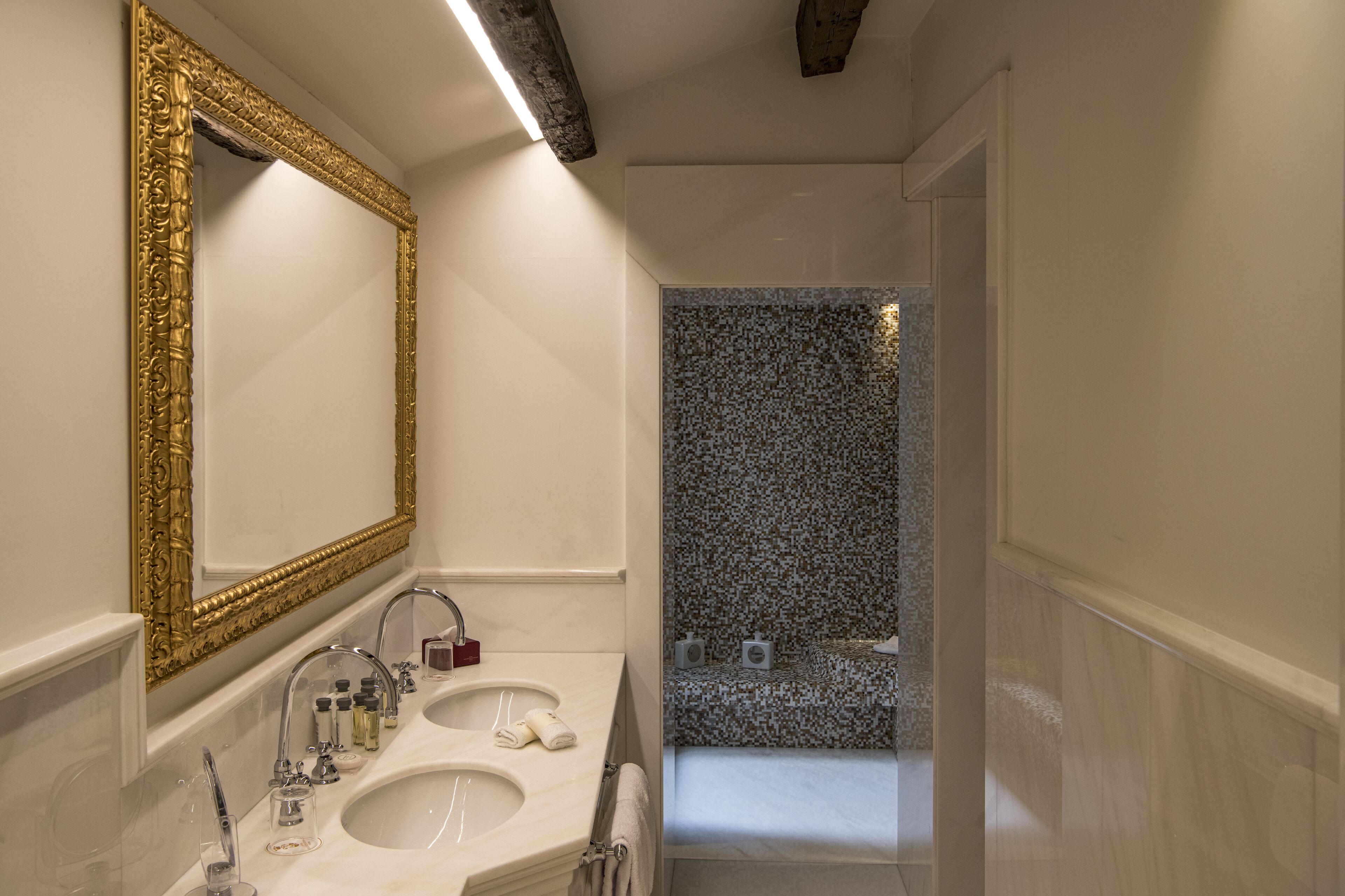 Ein Badezimmer mit einem großen, verzierten Spiegel, zwei Waschbecken und einer Duschkabine mit einem rauen Fliesenbelag.