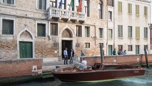 A wooden boat on a canal, a building with a green door, and people standing by the canal.