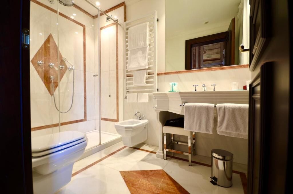 Une salle de bain moderne avec une douche à parois de verre, des toilettes blanches, un bidet, un lavabo avec un miroir et une poubelle.