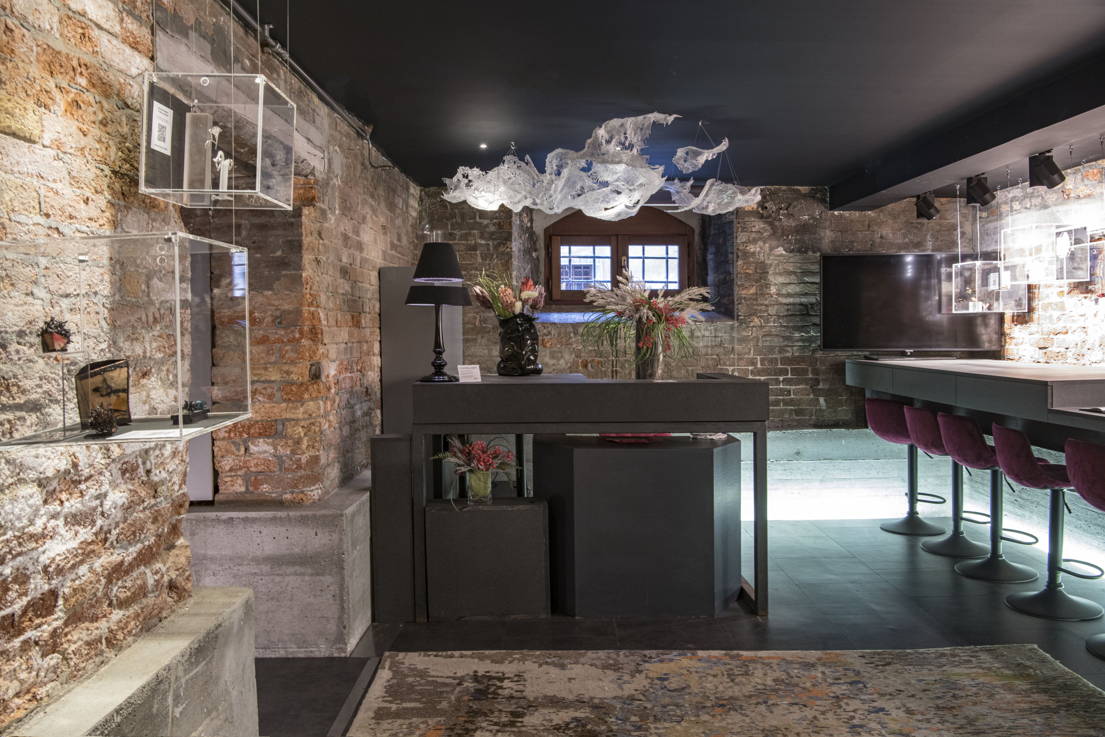 Una cocina moderna con paredes de ladrillo visto, una zona de bar con taburetes morados y elementos decorativos de cristal en el techo.