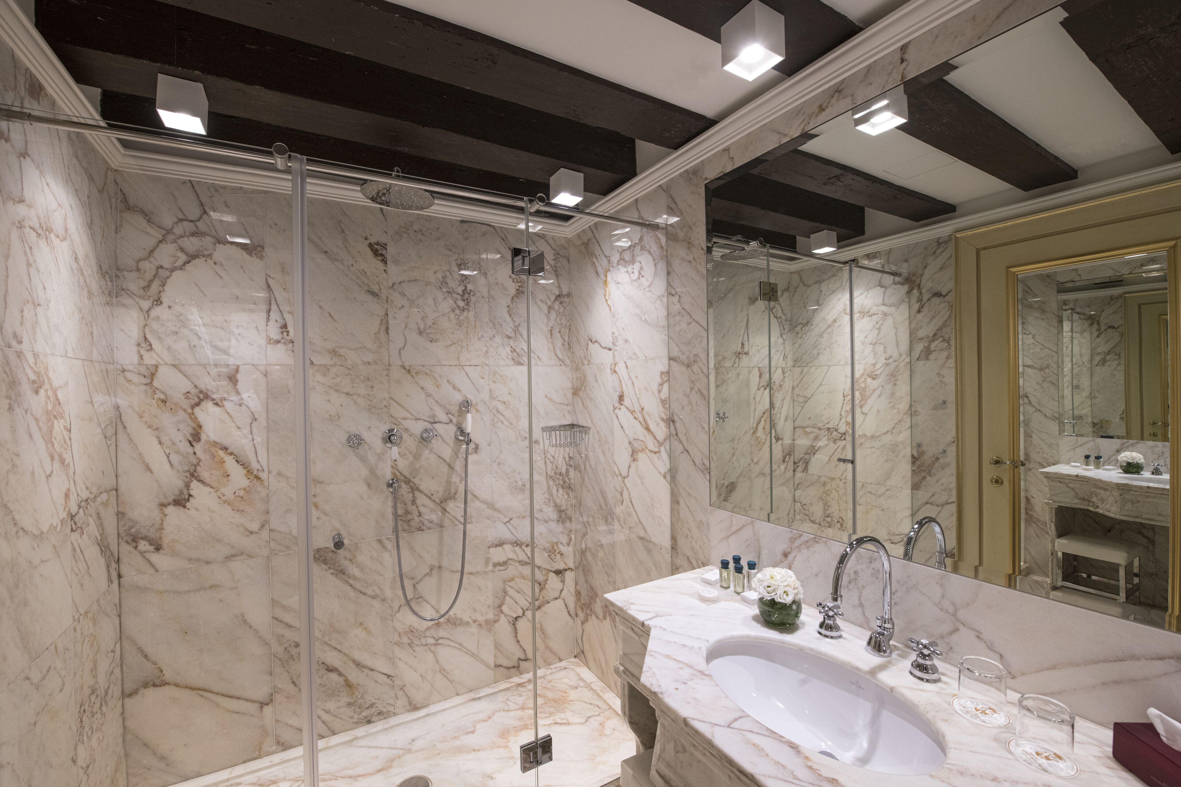 A modern bathroom with a marble sink, a large mirror, and a glass-enclosed shower.