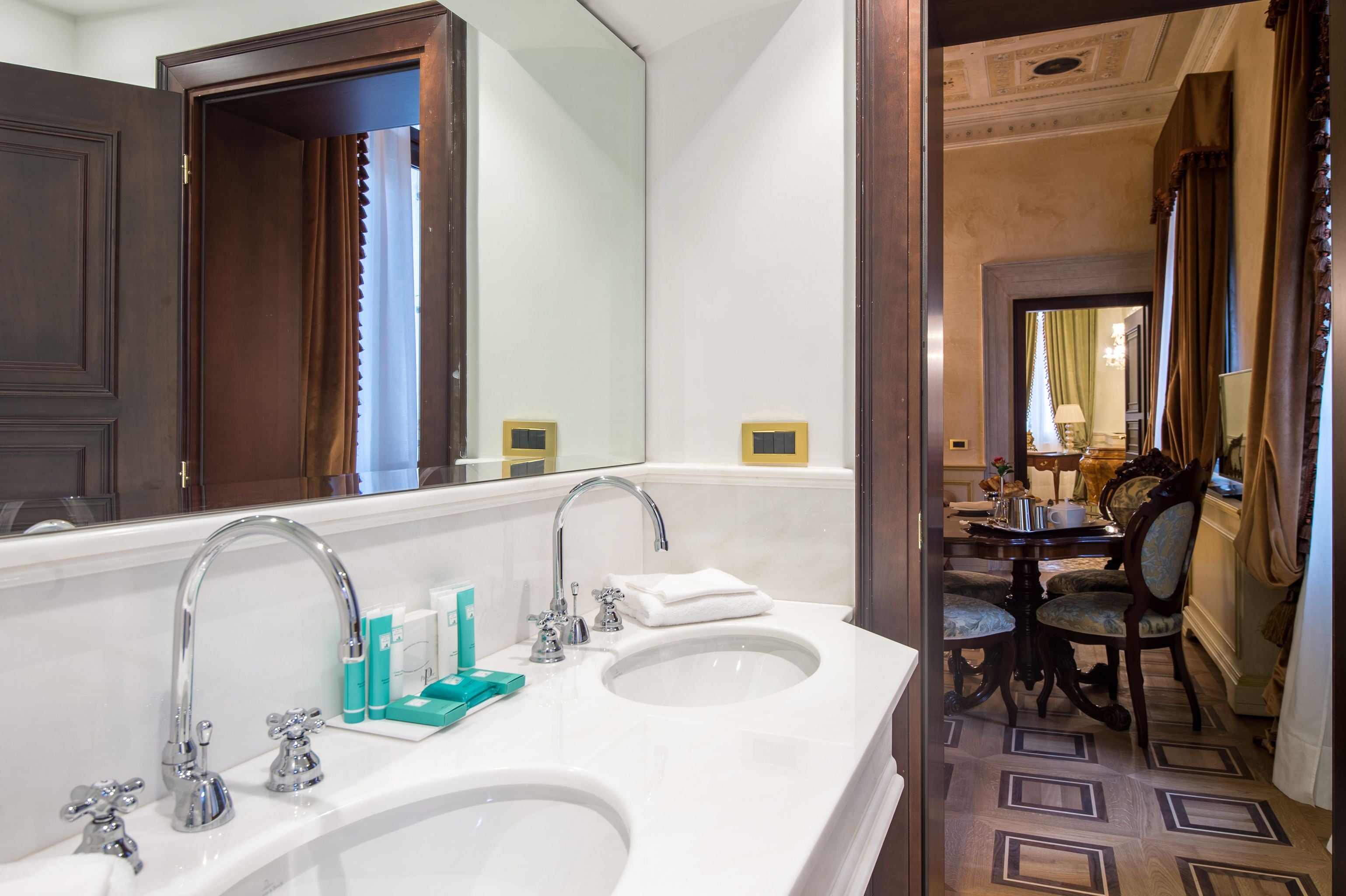 A bathroom with two sinks, a large mirror, and a dining area with a table and chairs.