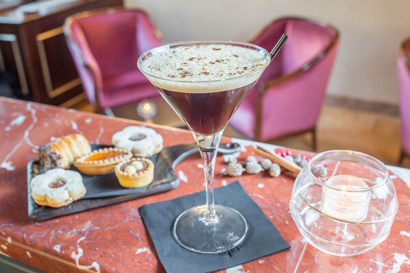 A martini glass with a frothy top on a marble table, accompanied by a small candle and assorted pastries. - Hotel Nani Mocenigo Palace (Venice)