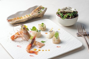 Un piatto di pesce con gamberi e capesante su un piatto bianco, accompagnato da un'insalata e una conchiglia con ostriche.