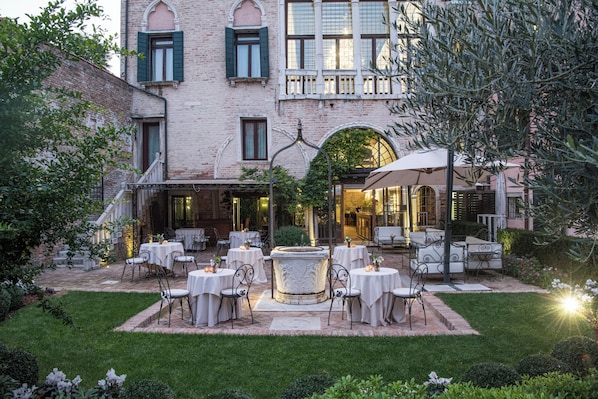 A courtyard with outdoor seating, a fountain, and a building with arched windows and a balcony. - Hotel Nani Mocenigo Palace (Venice)