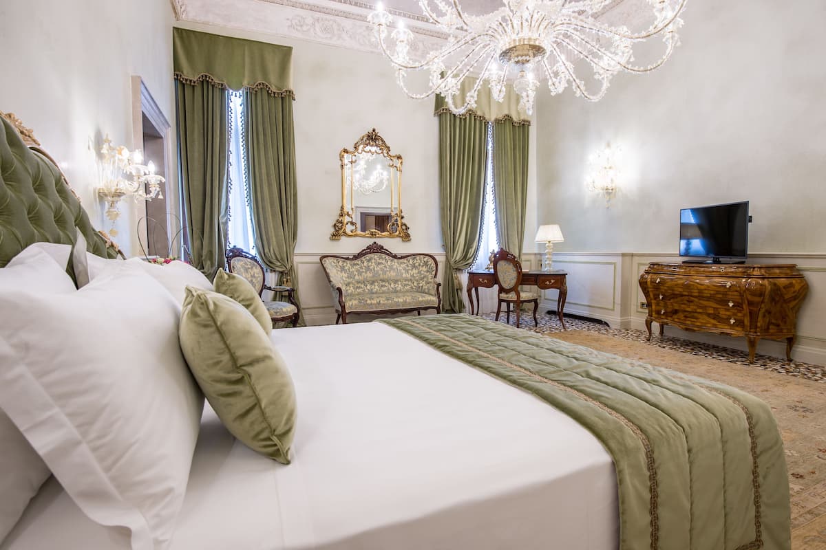 Ett hotellrum med en stor säng, en tv, en byrå och en kristallkrona.