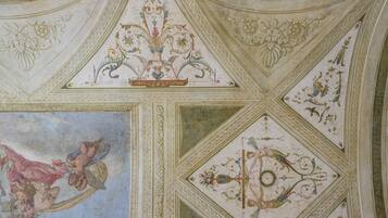A ceiling with intricate floral and geometric patterns, including a central medallion and a fresco of cherubs.
