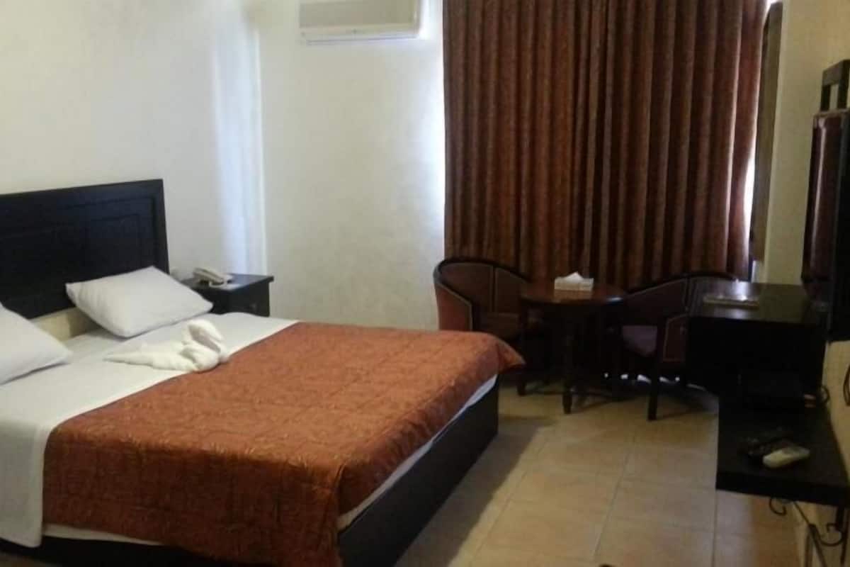A hotel room with a bed, a desk, a chair, a TV, and a window with curtains.