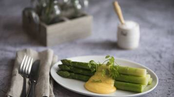 A plate of asparagus with a creamy sauce and a sprig of parsley, a fork and knife on a napkin, and a salt and pepper shaker in the background.