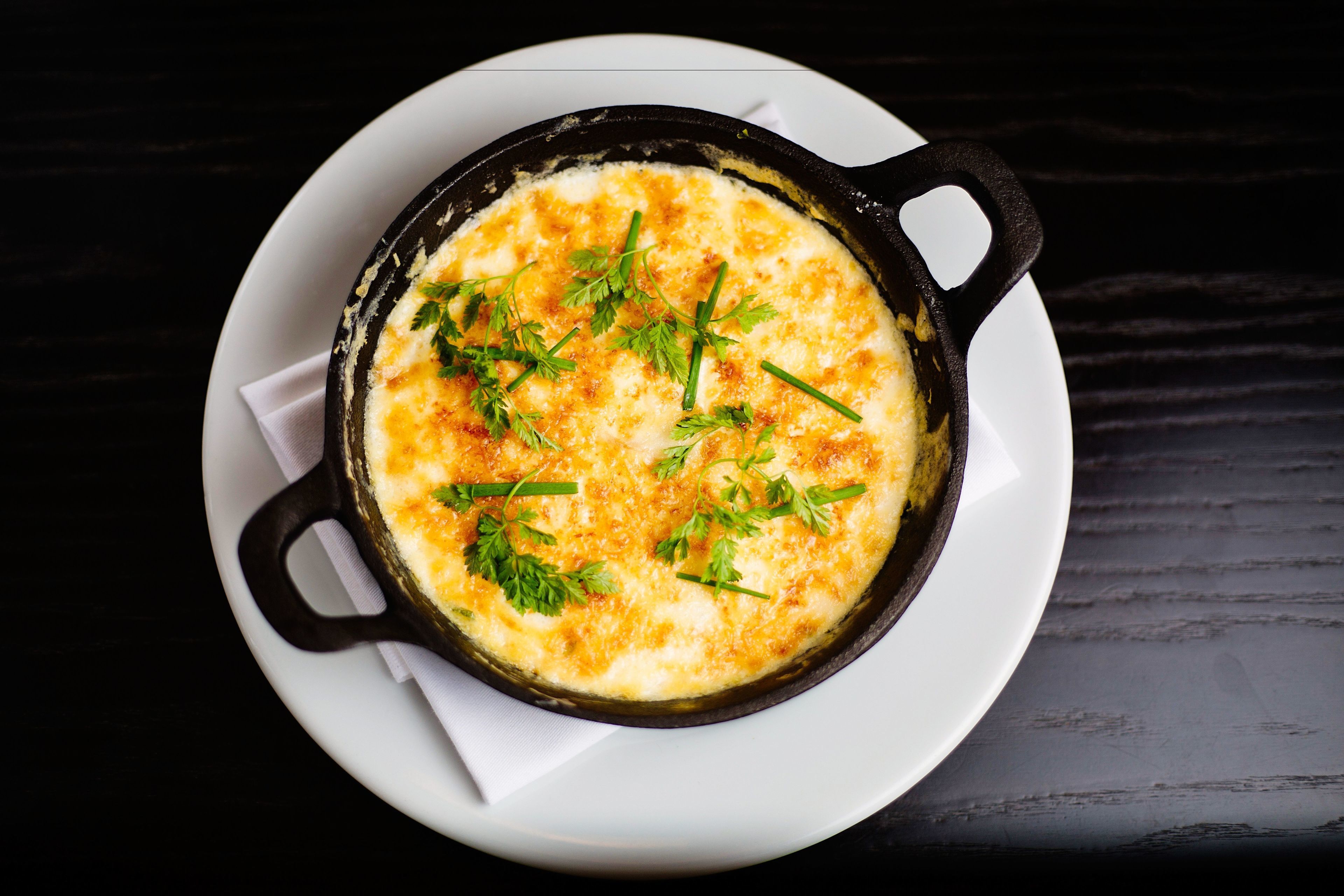 A dish in a cast iron skillet on a white plate with a napkin underneath.