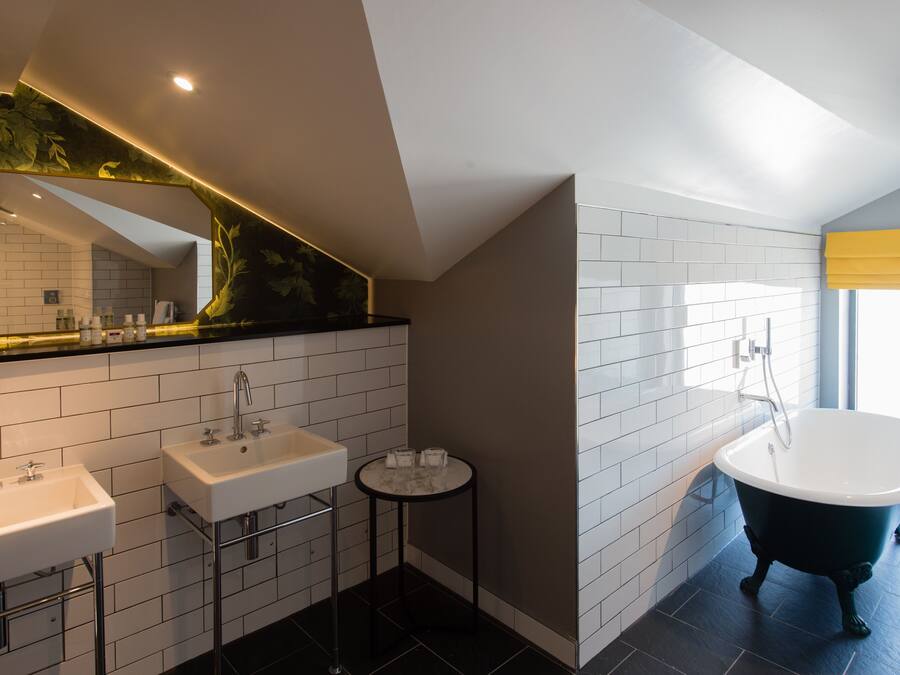 Une salle de bain moderne avec deux lavabos, un miroir rond, une baignoire et une petite table avec des verres.