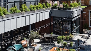 An outdoor patio area with tables and chairs, a bicycle, and a wooden planter box with plants. - Hotel Du Vin Stratford Upon Avon (Stratford-upon-Avon)