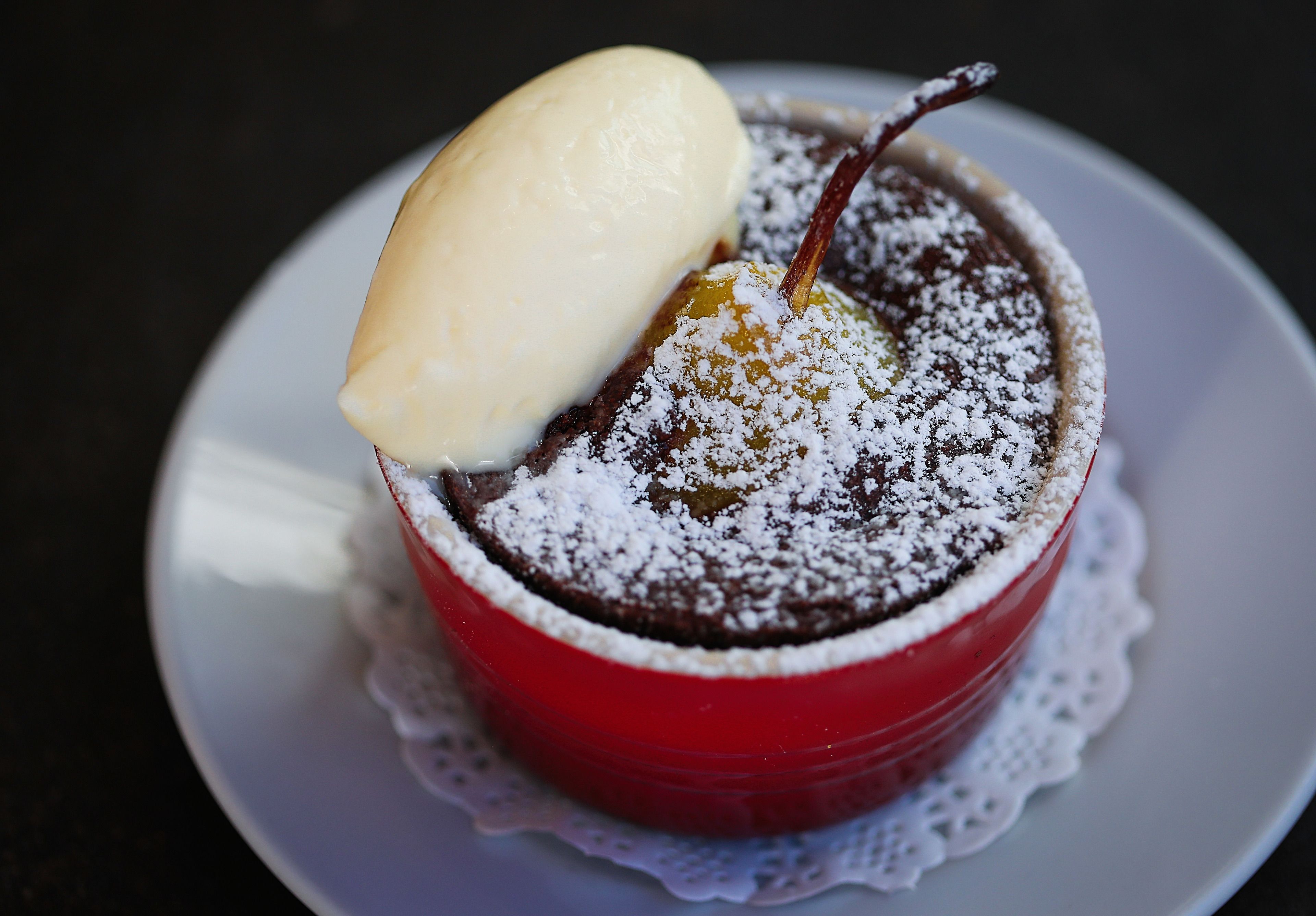 Un dessert servi dans un bol rouge, posé sur une assiette blanche, lui-même surmonté d’une petite nappe en dentelle.