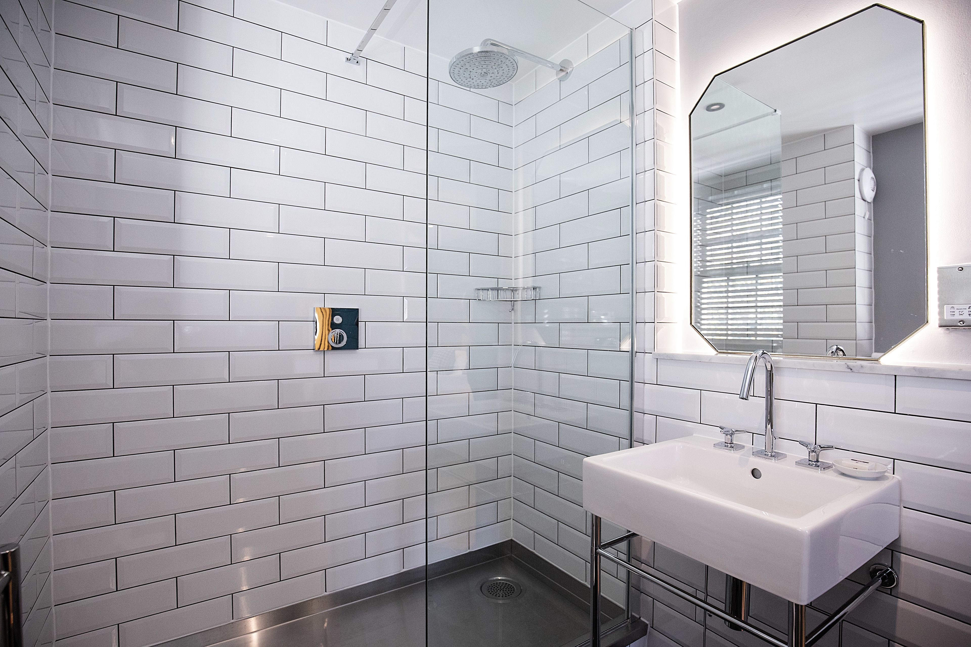 Un baño moderno con azulejos blancos tipo metro, cabina de ducha con cristal, lavamanos blanco y espejo.