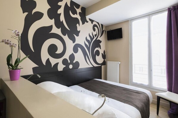 A hotel room with a bed, a potted plant, a TV, and a window with curtains.