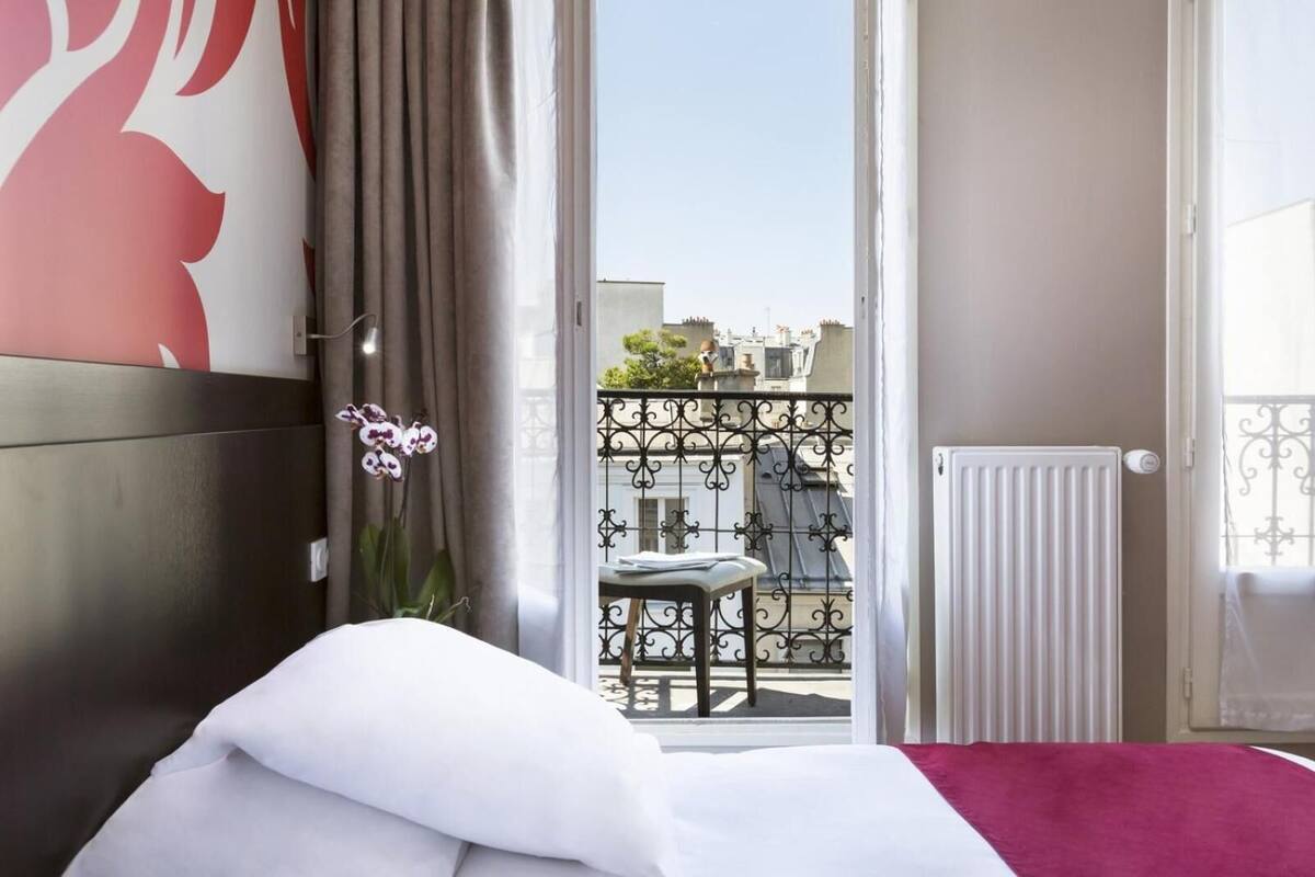 Una habitación de hotel con una cama, vistas al balcón y un ventanal con cortinas.