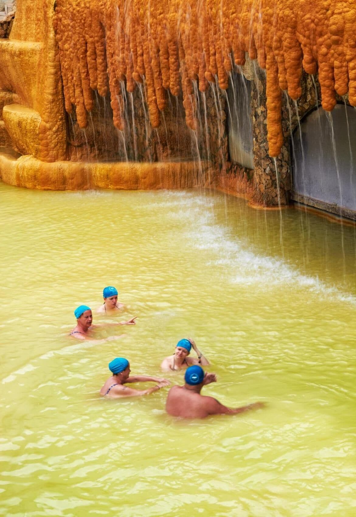 A group of people in a pool with a unique geological formation in the background.