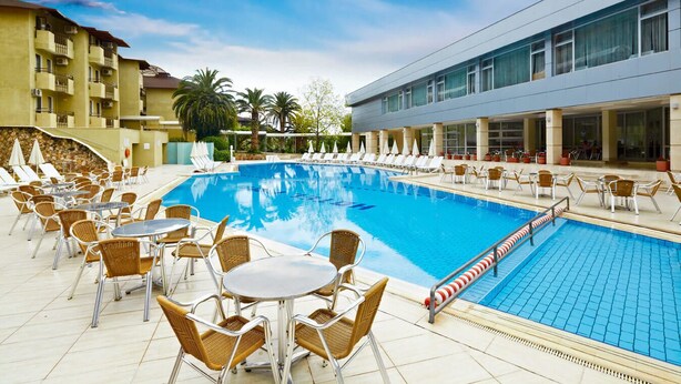 Una piscina con sillas y mesas de descanso, rodeada por un edificio con balcones.