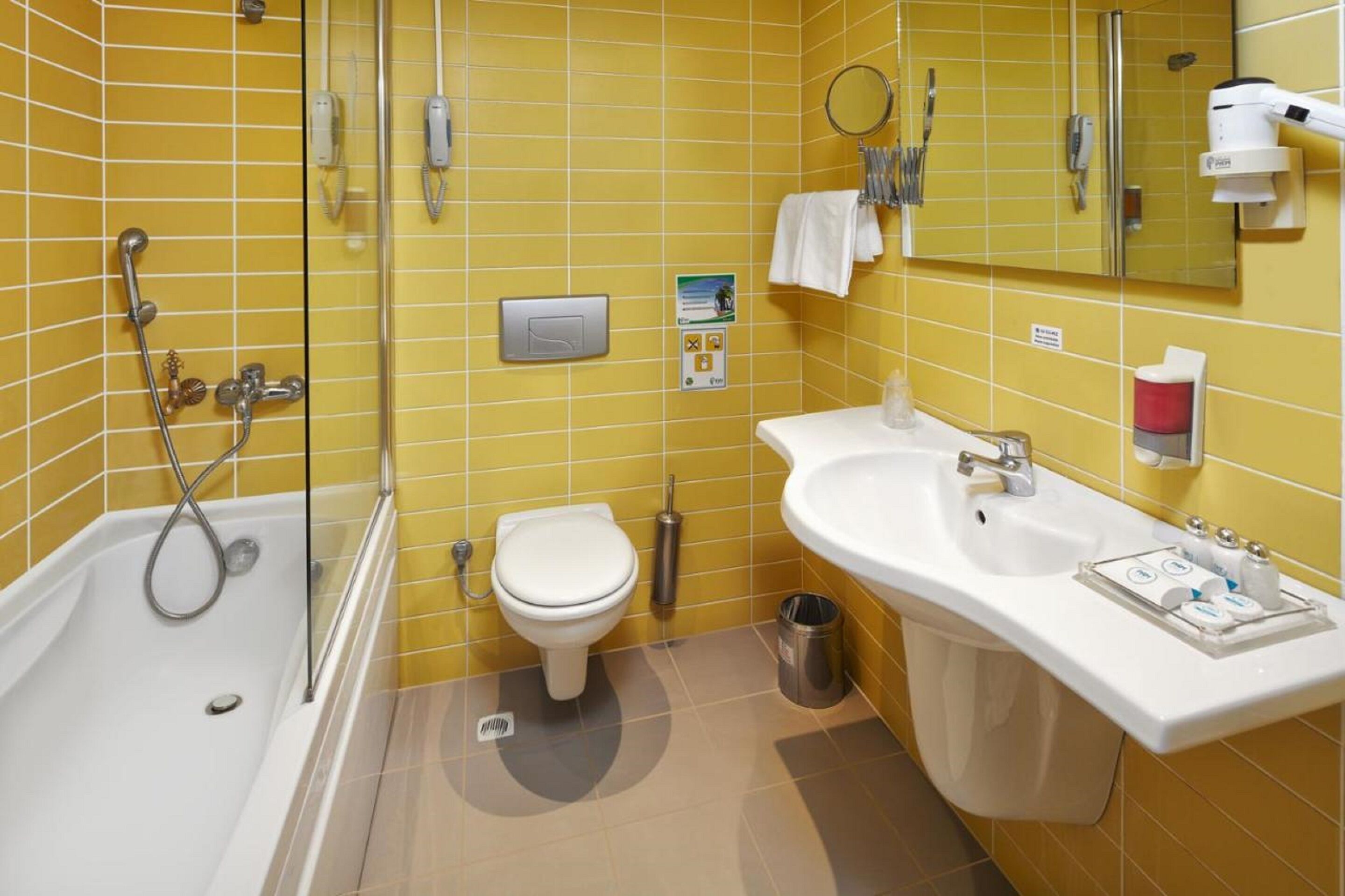 A bathroom with yellow tiled walls, a bathtub, a toilet, a sink, and a mirror.