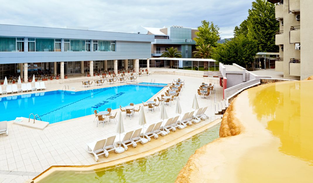 A pool area with lounge chairs and umbrellas, a building with large windows, and a clear sky.