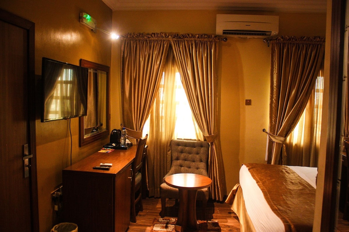 A hotel room with a bed, a desk, a chair, a small round table, and curtains.