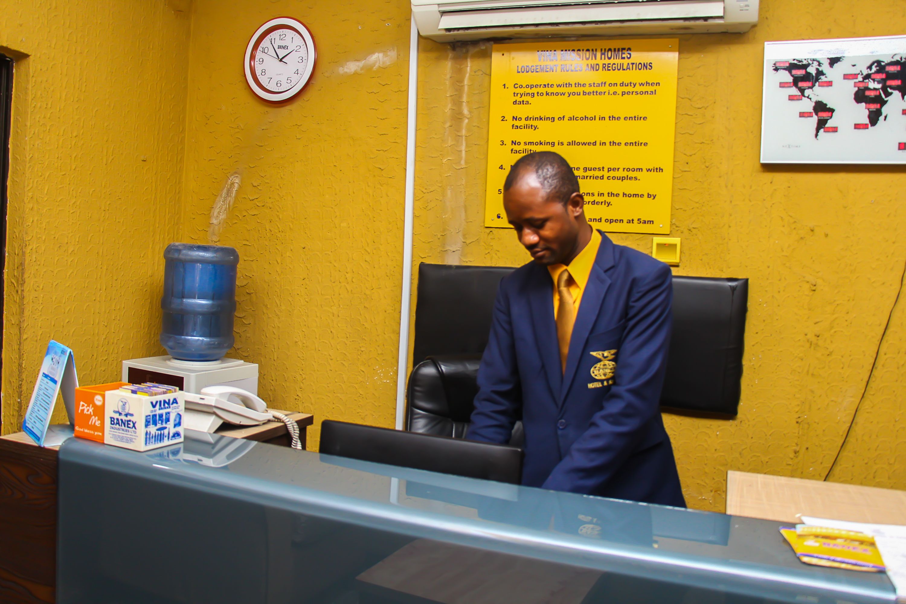 A reception desk with a clock, a water dispenser, and a sign listing room regulations.