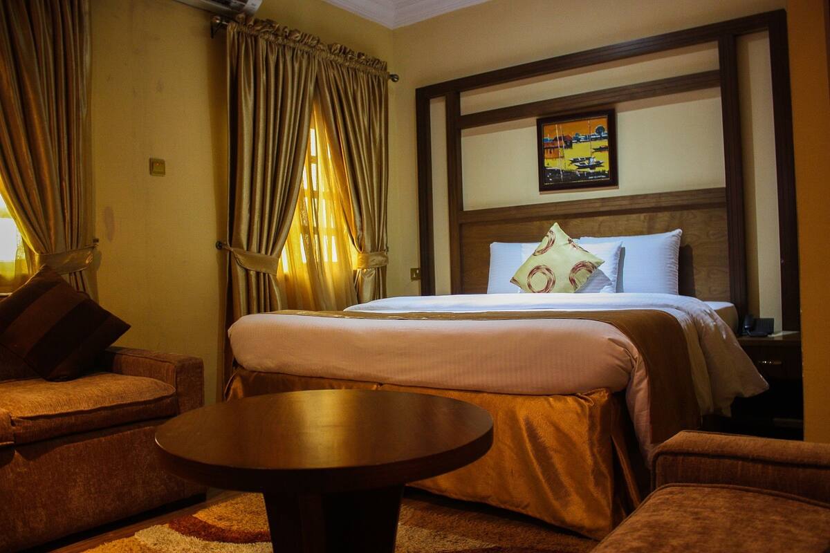 A hotel room with a large bed, a sofa, a small table, and curtains.